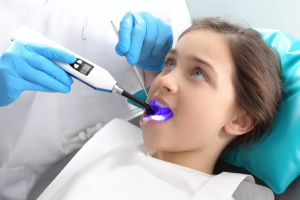 A dentist cleans a young girl's teeth, utilizing advanced laser cavity detection for optimal care.