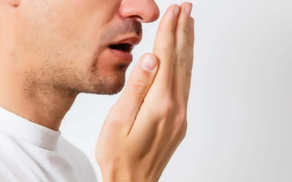 A man covers his mouth with his hand, indicating concern about his bad breath.