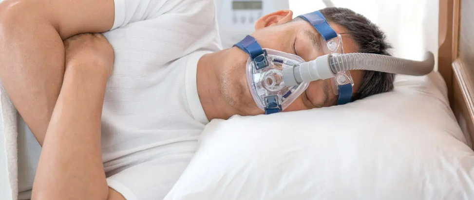 A man sleeping with a breathing mask, illustrating sleep apnea treatment.
